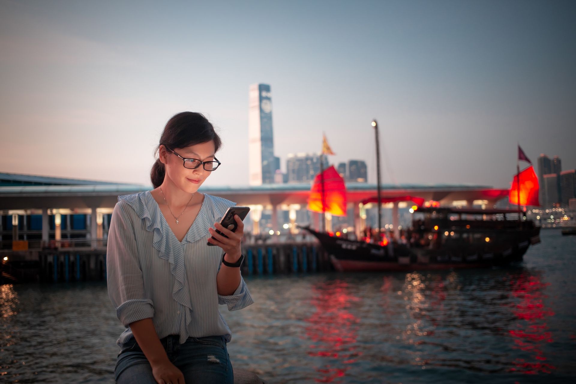 Girl using smartphone in Hong Kong Victoria Harbor with junk boat in background